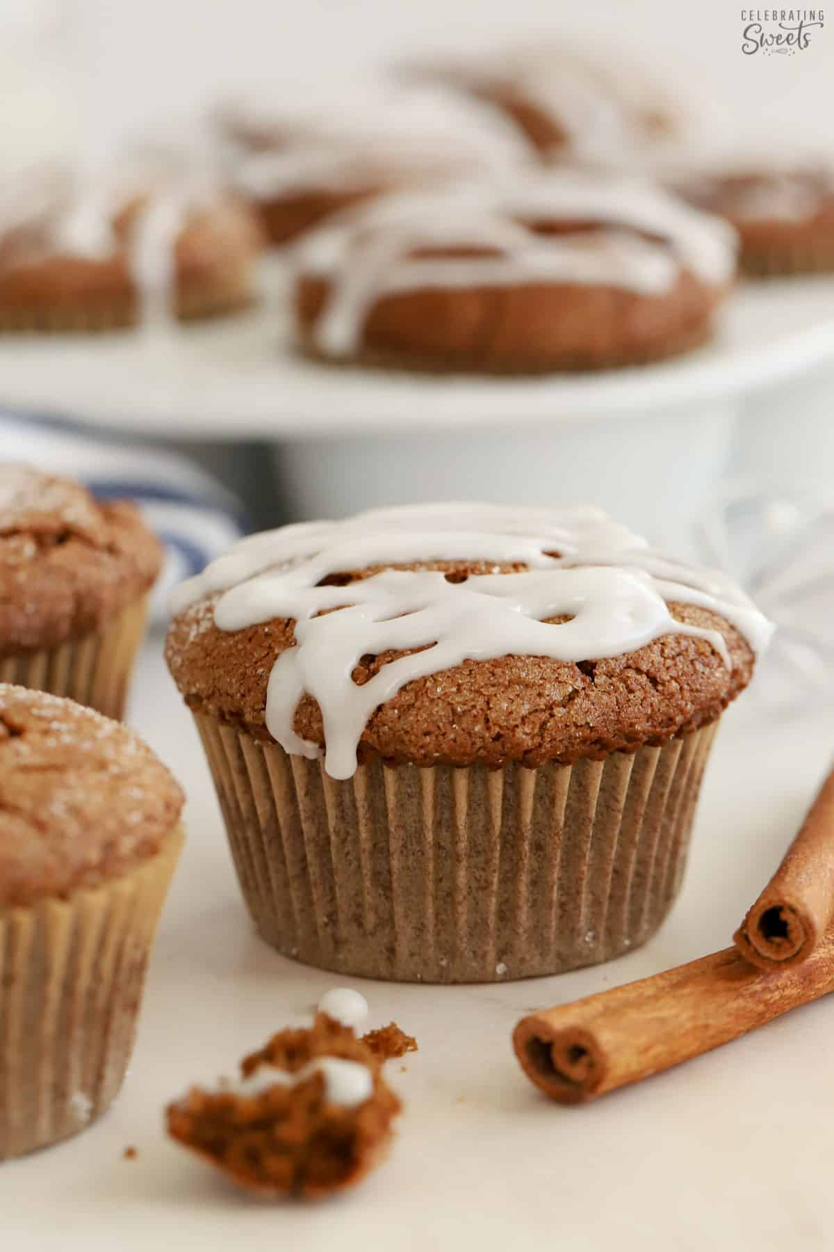 Gingerbread muffins topped with white icing next to two cinnamon sticks.