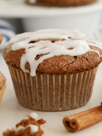 Gingerbread muffins topped with white icing next to two cinnamon sticks.