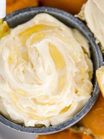 Closeup of honey butter in a blue bowl next to a plate of dinner rolls.