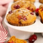 Pumpkin Cranberry Muffins in a white muffin pan next to a red and white striped towel.