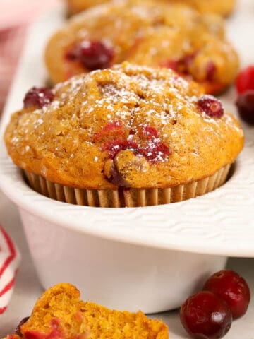 Pumpkin Cranberry Muffins in a white muffin pan next to a red and white striped towel.