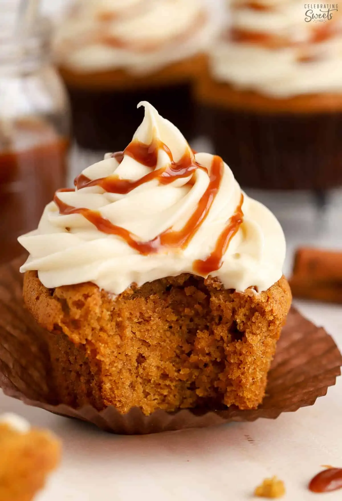 Pumpkin cupcake topped with frosting and caramel with a bite taken out of it.