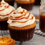 Pumpkin cupcake on a wire rack topped with white frosting and caramel.