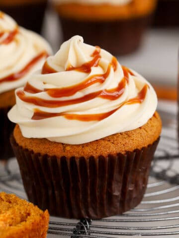 Pumpkin cupcake on a wire rack topped with white frosting and caramel.