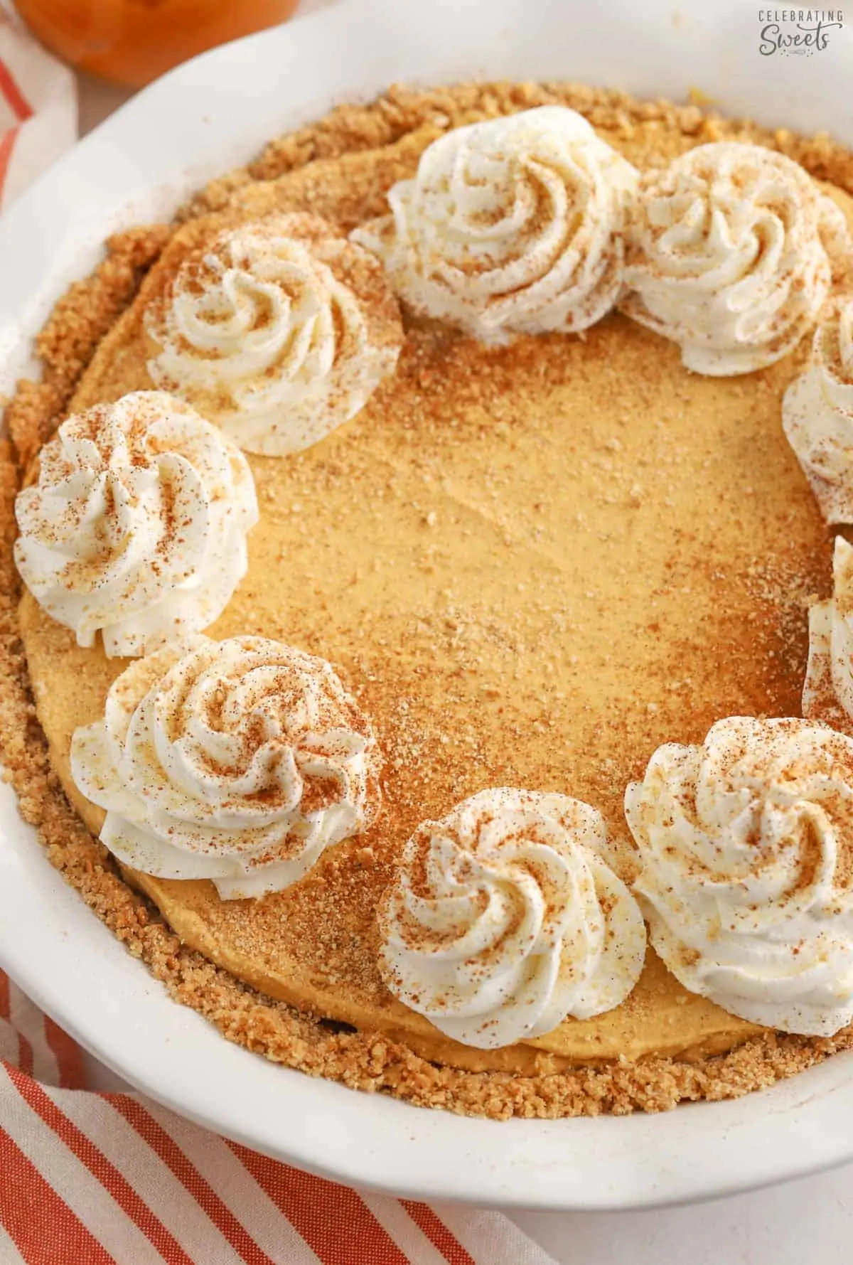 Pumpkin pie cheesecake topped with swirls of whipped cream and sprinkled with cinnamon sugar.
