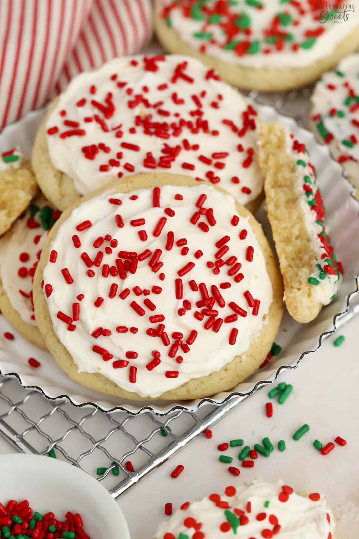 Sugar cookies topped with white frosting and red and green sprinkles on a wire rack.