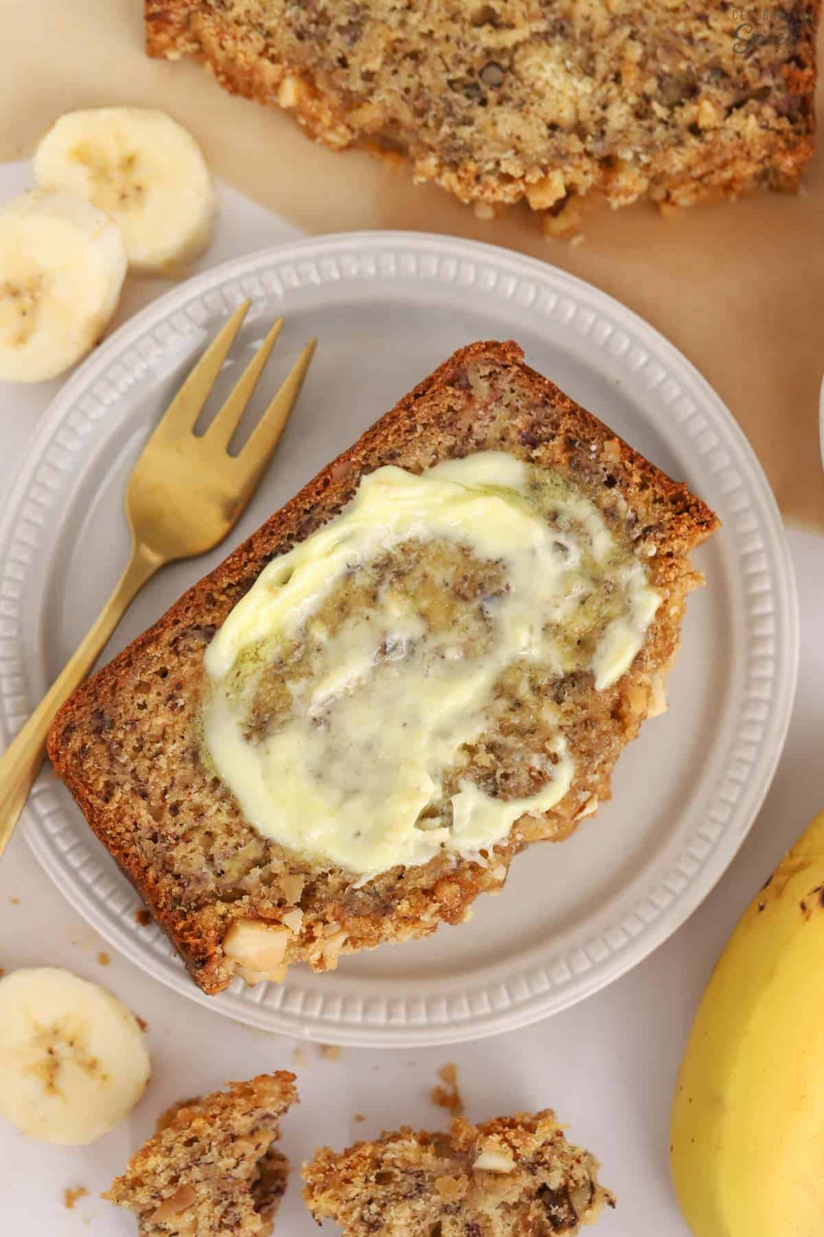 Slice of banana nut bread topped with butter on a grey plate.
