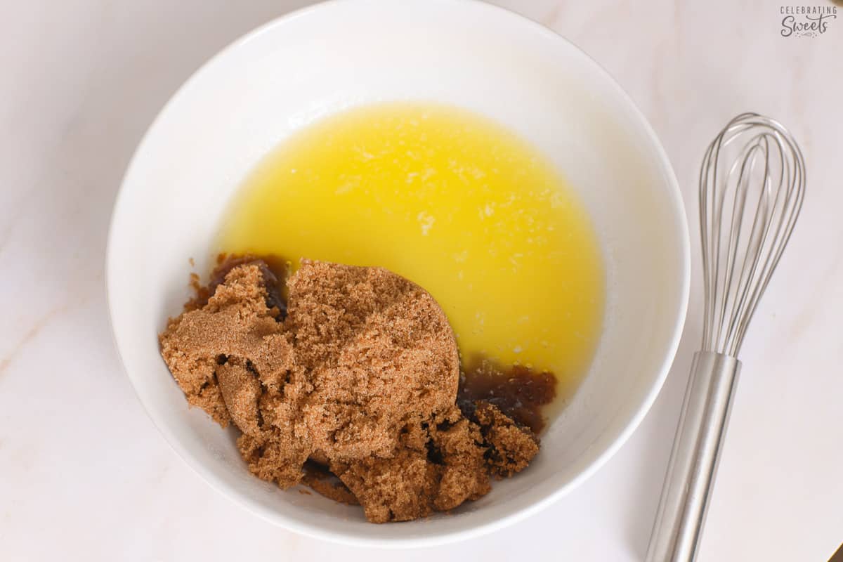 Butter and brown sugar in a white bowl next to a whisk.