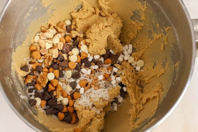 Cookie dough in a mixing bowl with chocolate chips, nuts, and coconut.