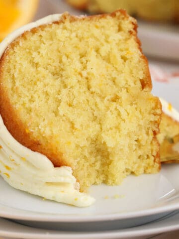 Slice of orange bundt cake on a white plate with a gold fork.