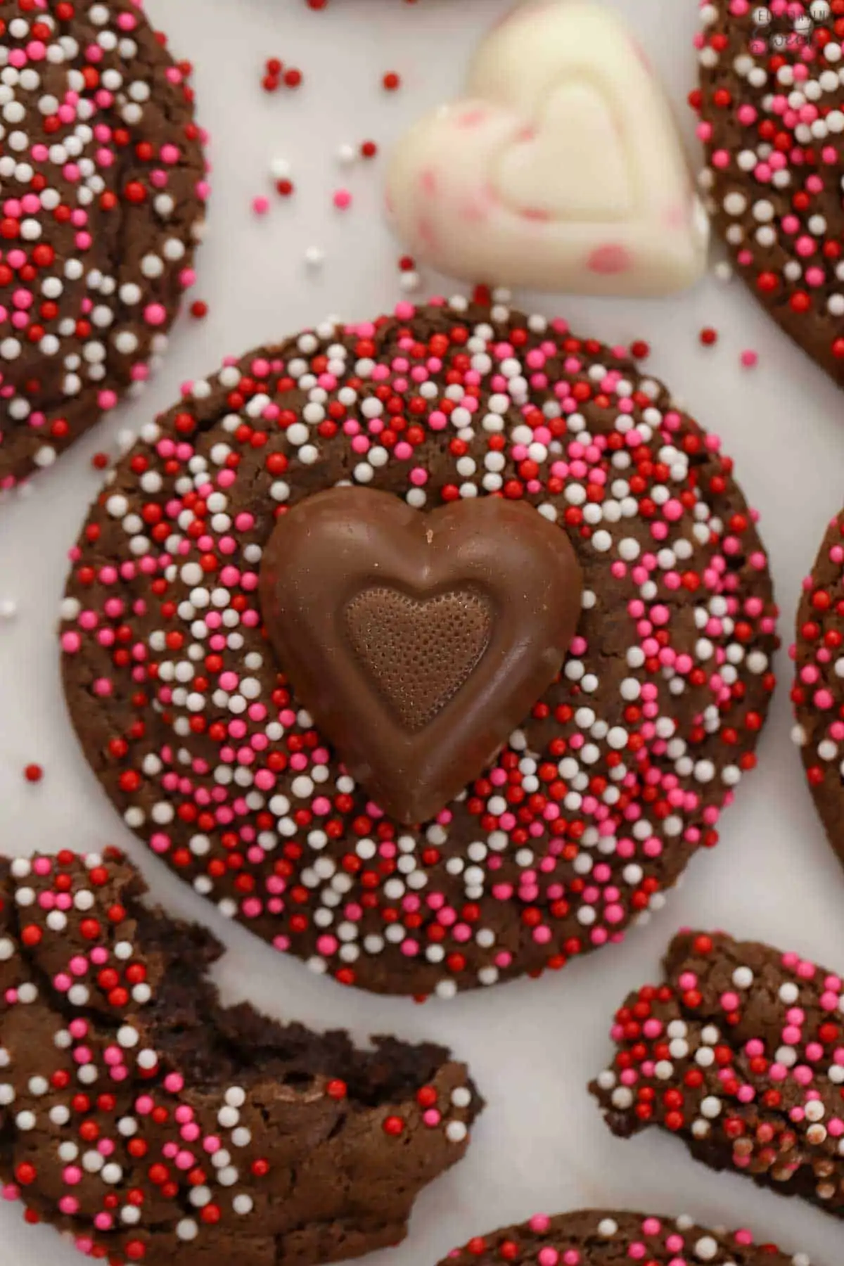 Chocolate cookies covered in red and pink sprinkles topped with chocolate hearts.