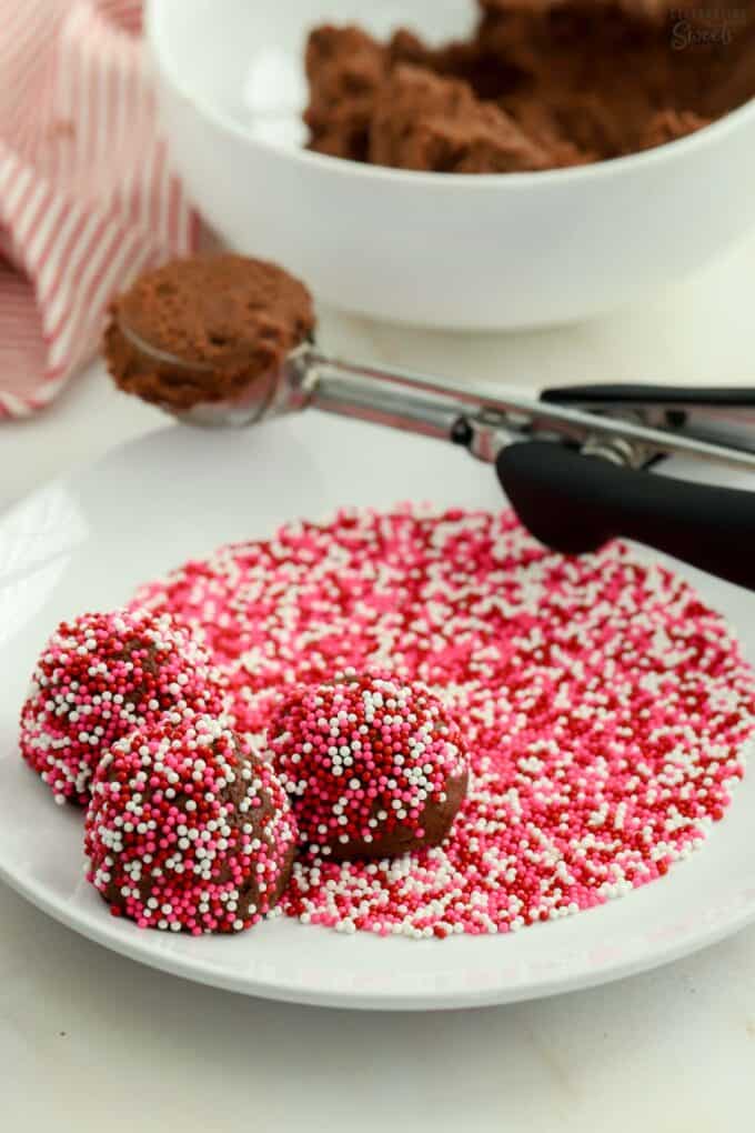 Chocolate cookie dough balls on a plate of pink and red sprinkles.