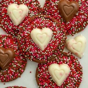 Chocolate cookies covered in red and pink sprinkles topped with chocolate hearts.