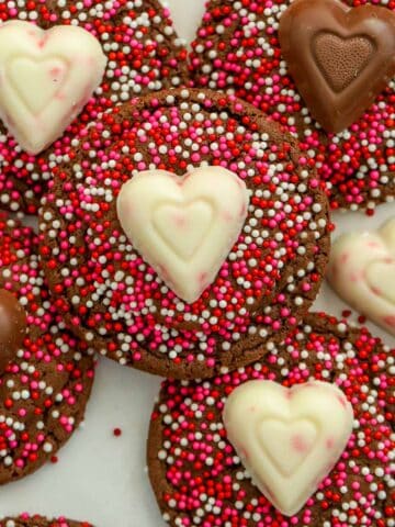 Chocolate cookies covered in red and pink sprinkles topped with chocolate hearts.