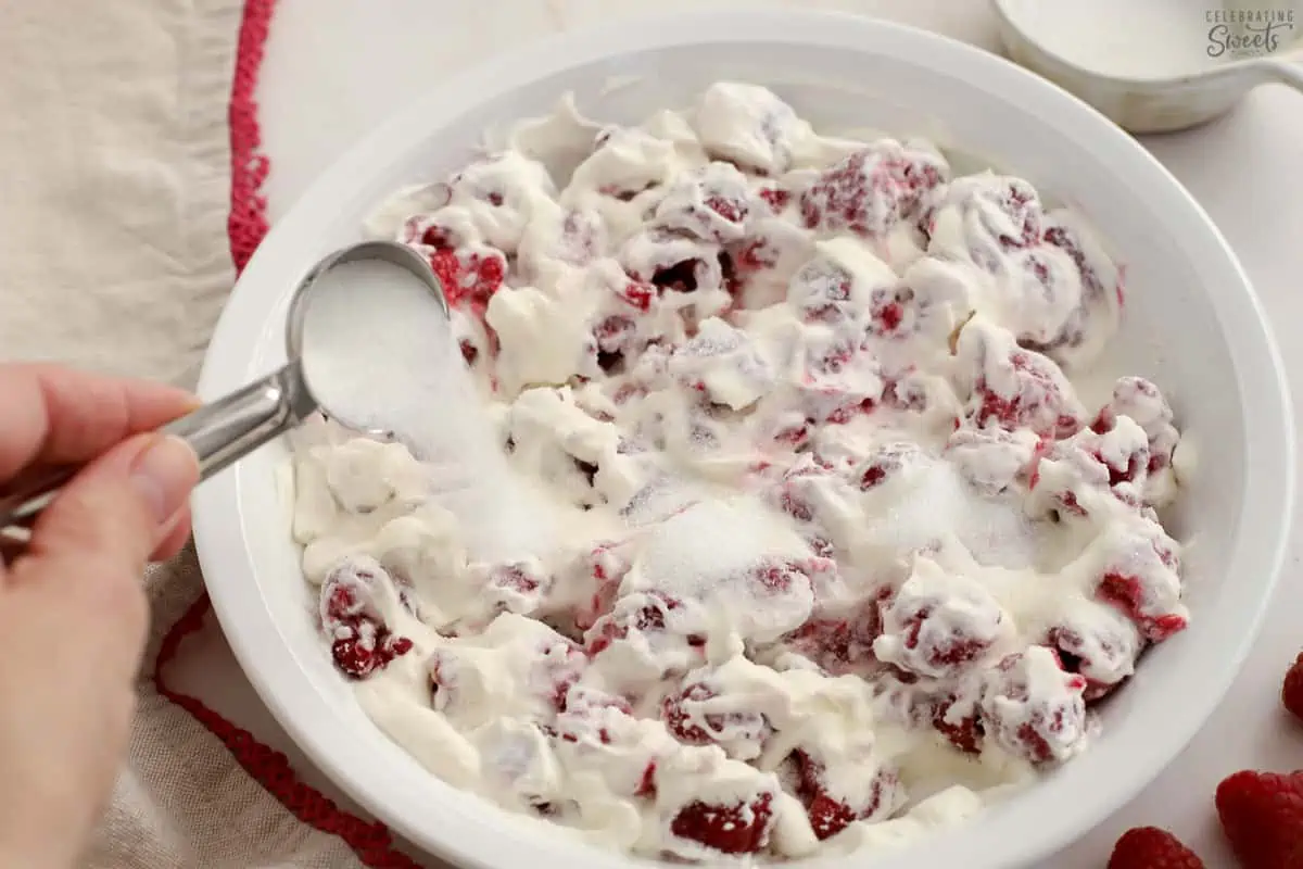Raspberries, whipped cream, and sugar in a white baking dish.
