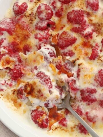 Berries, whipped cream, and caramelized sugar in a white baking dish.