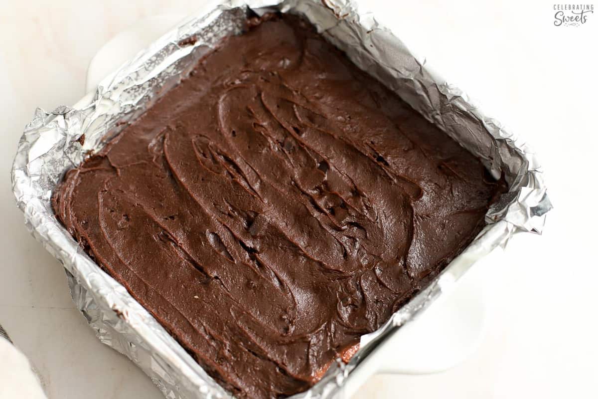 Brownie batter in a foil-lined square pan.