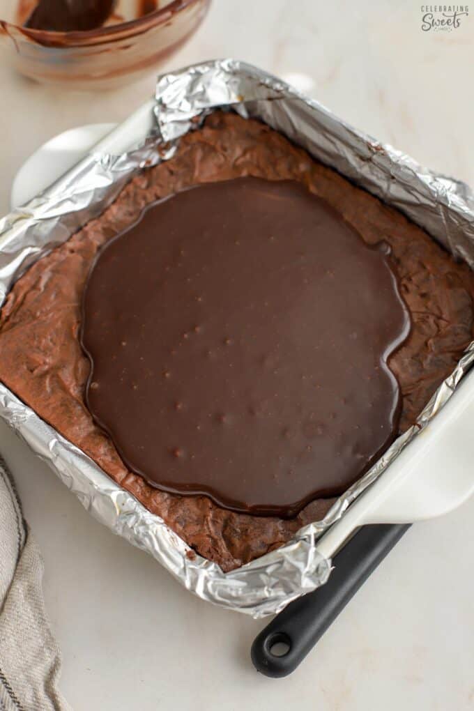 Brownies topped with chocolate ganache in a foil-lined pan.