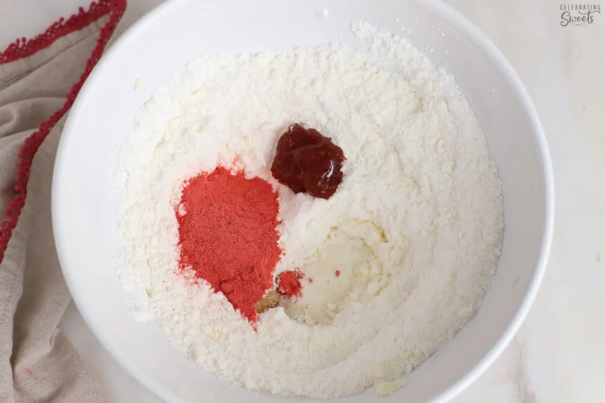 Butter, powdered sugar, jam, and freeze dried strawberries in a white bowl.