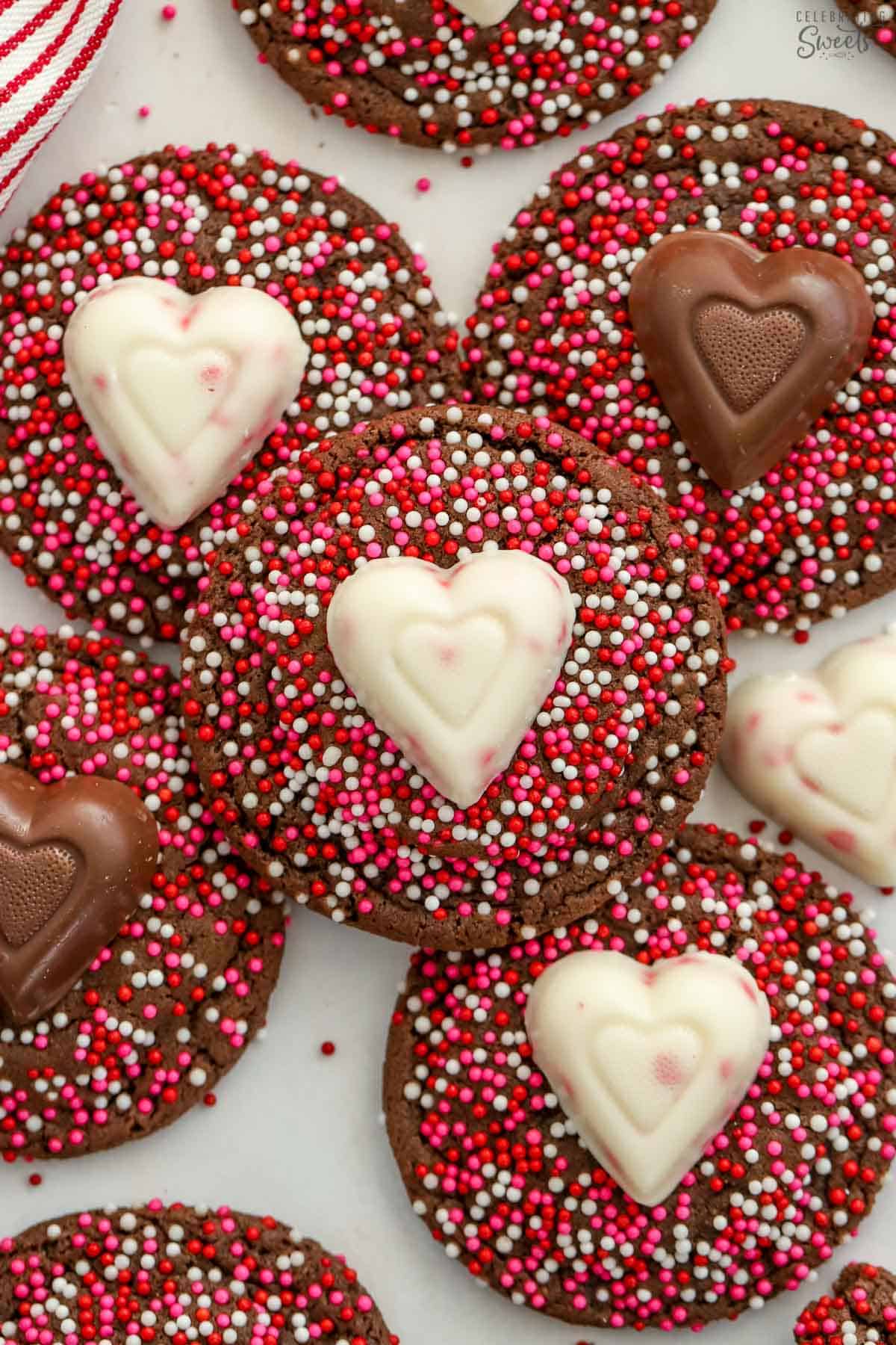 Chocolate cookies covered in pink and red sprinkles topped with a candy heart.