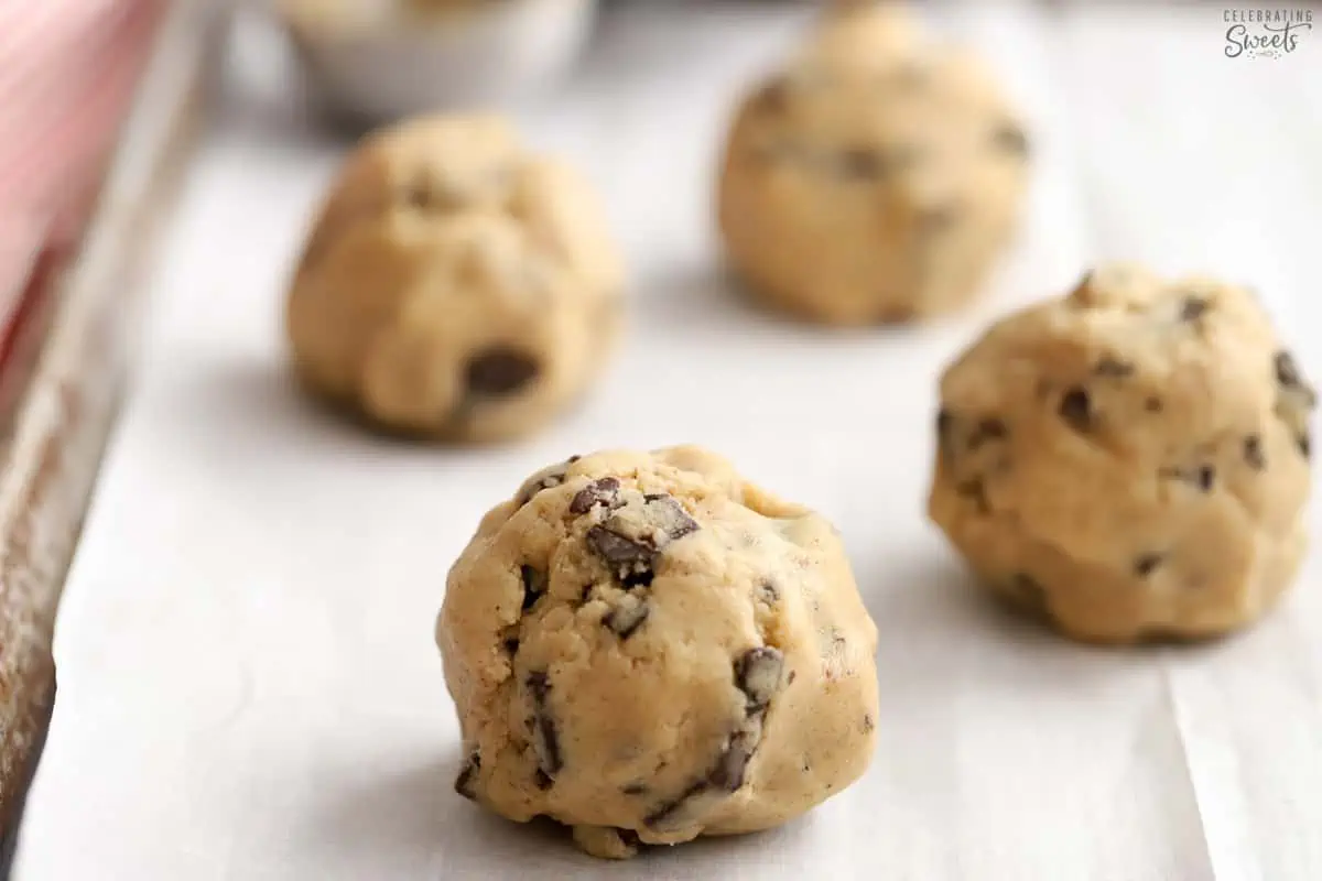 Large cookie dough balls on a parchment lined baking sheet.