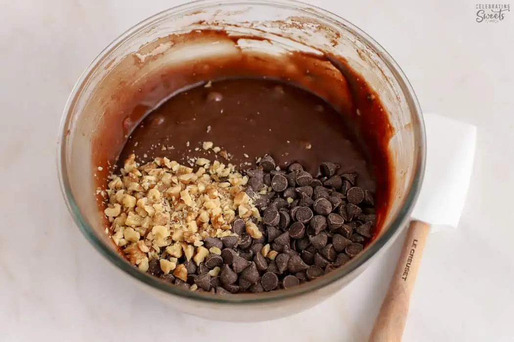 Brownie batter, chocolate chips, and nuts in a glass bowl.