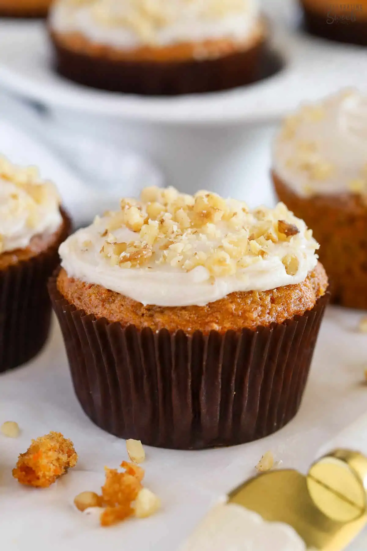 Carrot muffin topped with frosting and chopped walnuts.