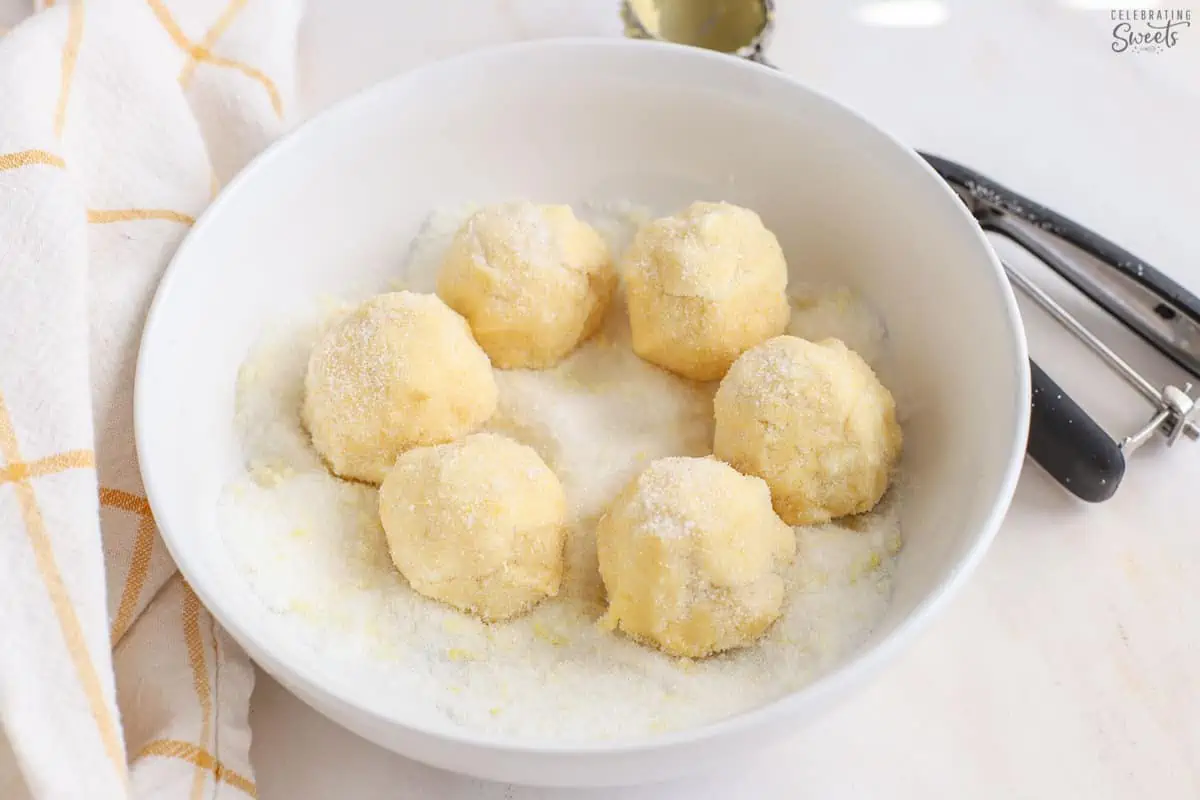 Cookie dough balls in a bowl of sugar and lemon zest.