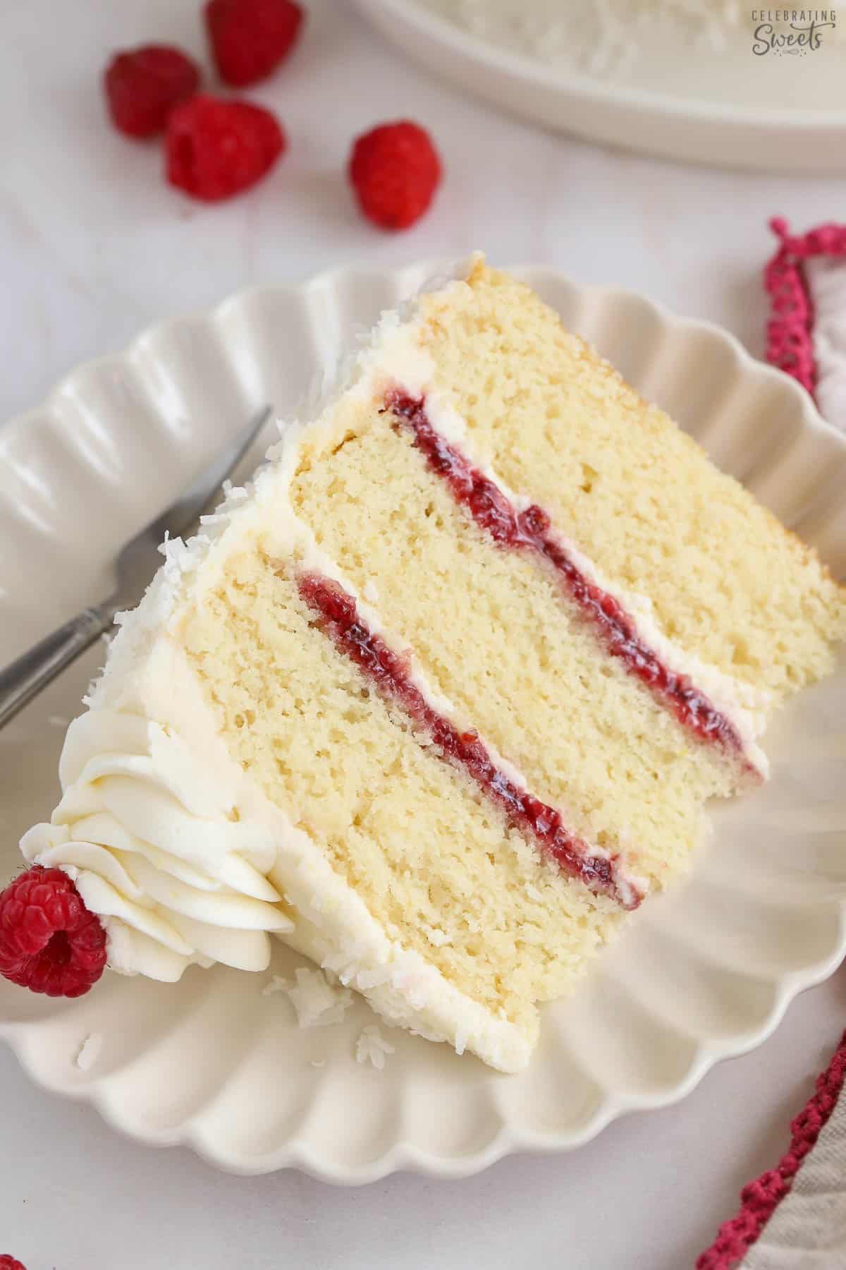 Slice of white cake topped with white frosting and filled with raspberry jam.