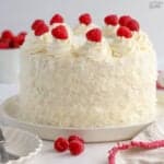 White layer cake topped with raspberries and covered in shredded coconut.