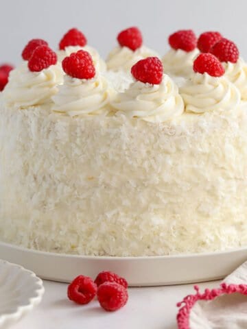 White layer cake topped with raspberries and covered in shredded coconut.