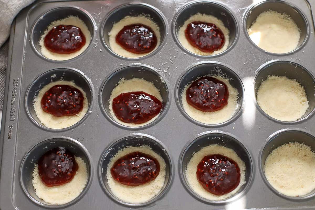 Crumb dough and raspberry jam in a muffin tin.