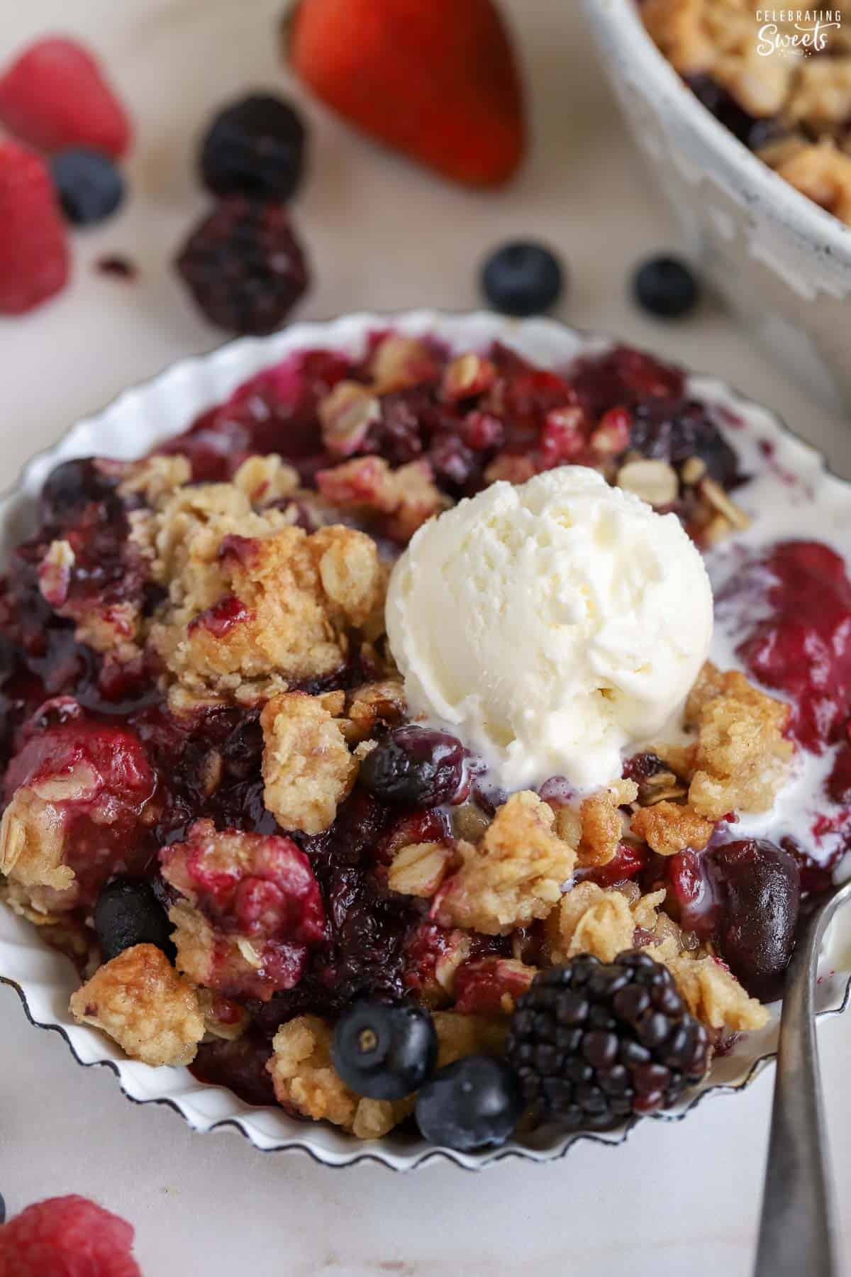 Berry crisp topped with ice cream in a white bowl.
