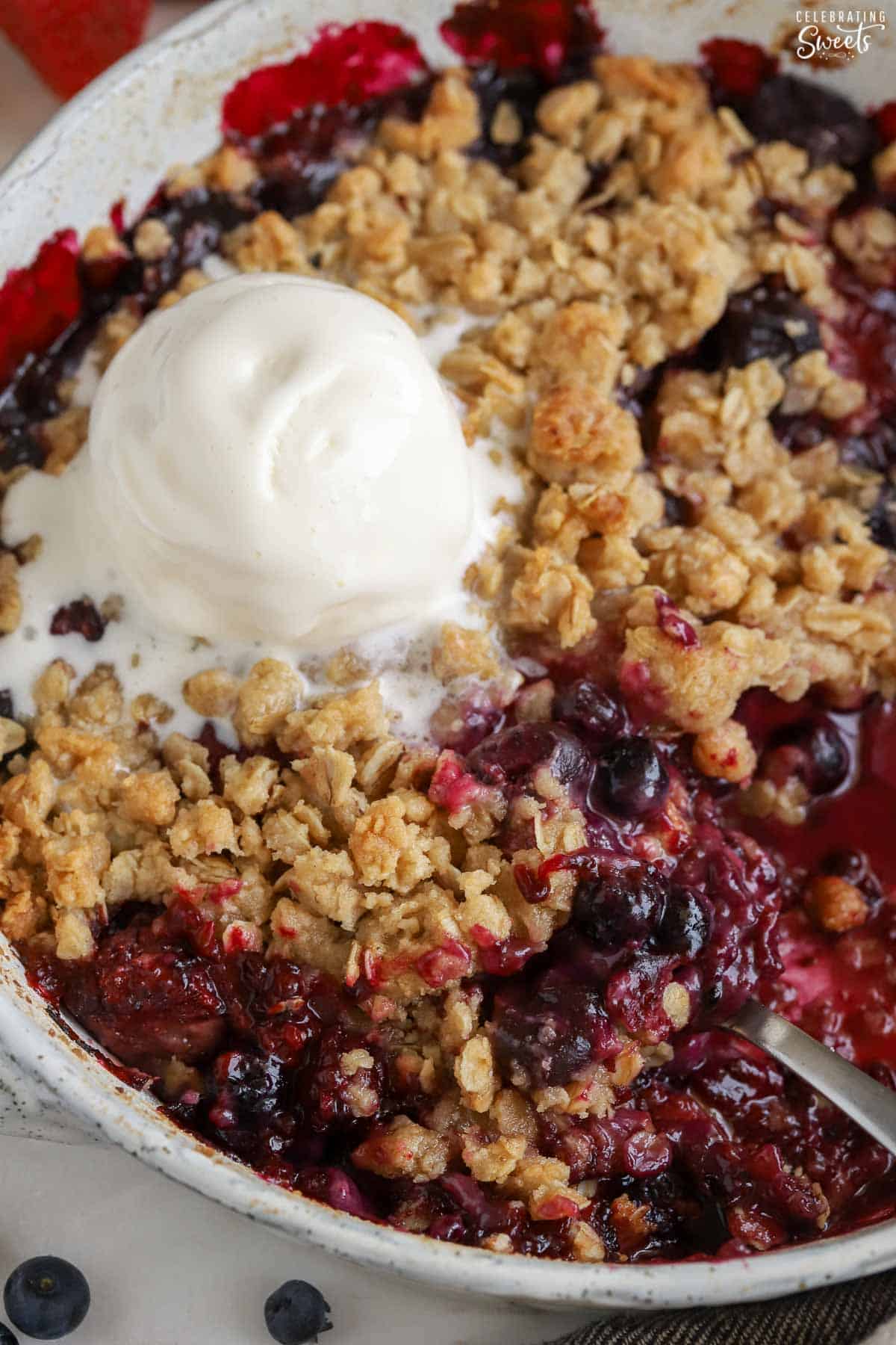 Berry crisp topped with ice cream in a baking dish.