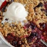 Berry crisp topped with ice cream in a baking dish.