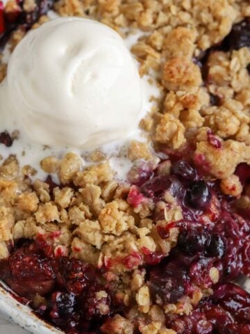 Berry crisp topped with ice cream in a baking dish.