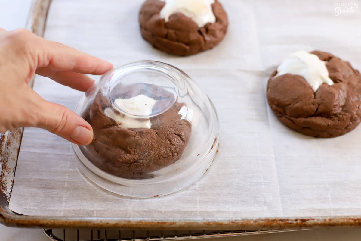 A glass bowl over the top of a chocolate cookie on a baking sheet.