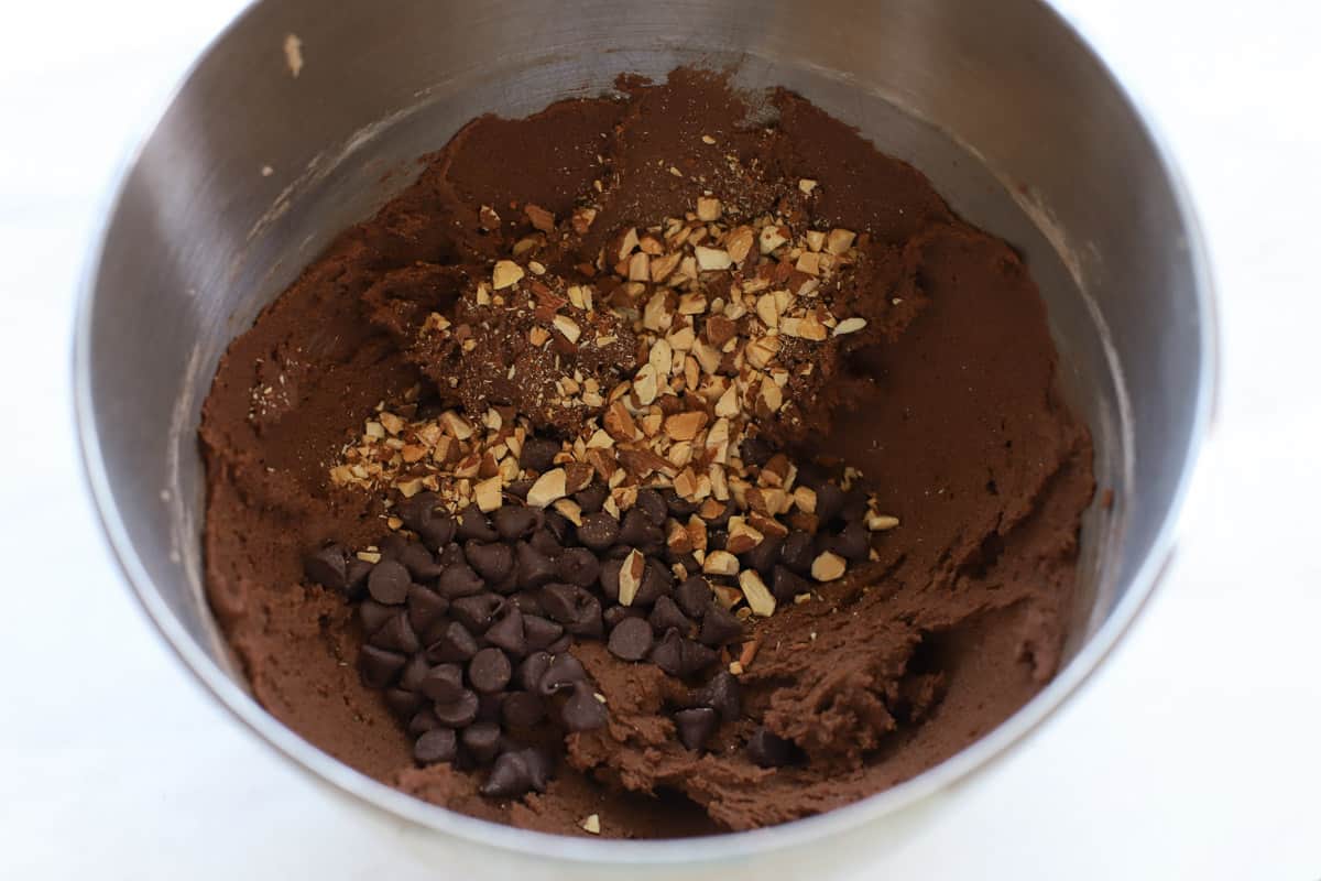 Chopped nuts and chocolate chips in a bowl of chocolate cookie dough.