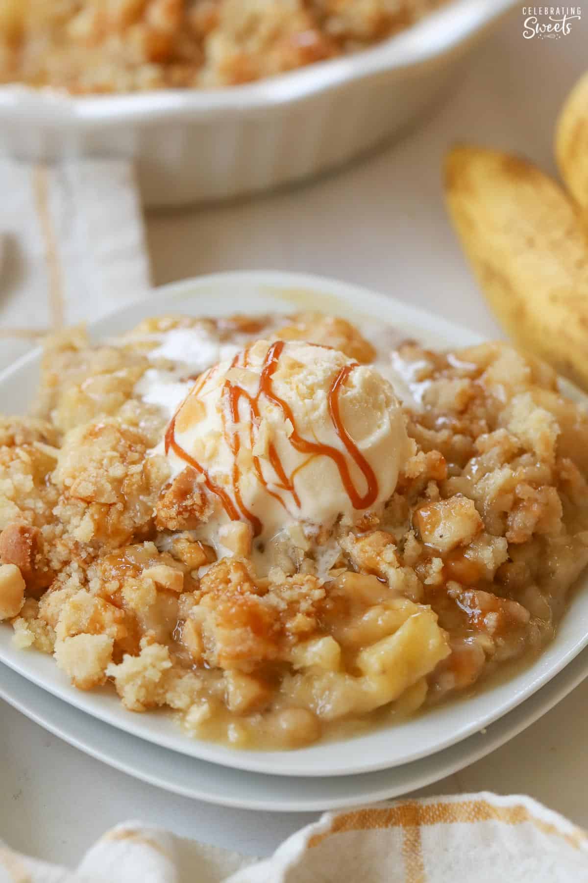 Banana crumble topped with caramel drizzle and vanilla ice cream on a white plate.