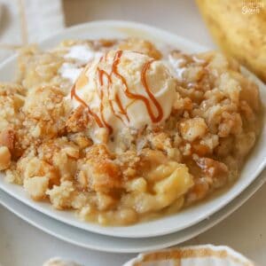 Banana crumble topped with caramel drizzle and vanilla ice cream on a white plate.
