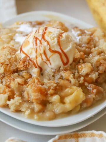 Banana crumble topped with caramel drizzle and vanilla ice cream on a white plate.