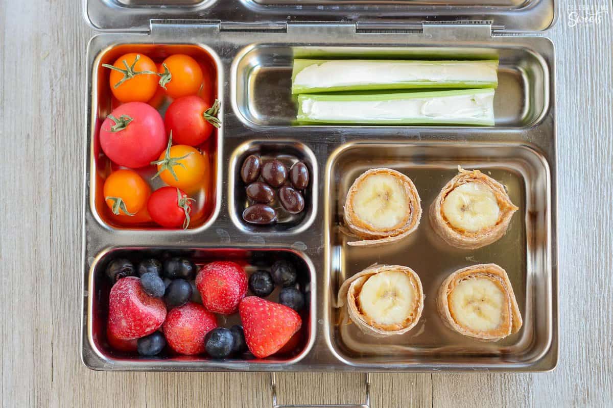 Lunchbox filled with banana roll ups fruit, veggies, and chocolate.