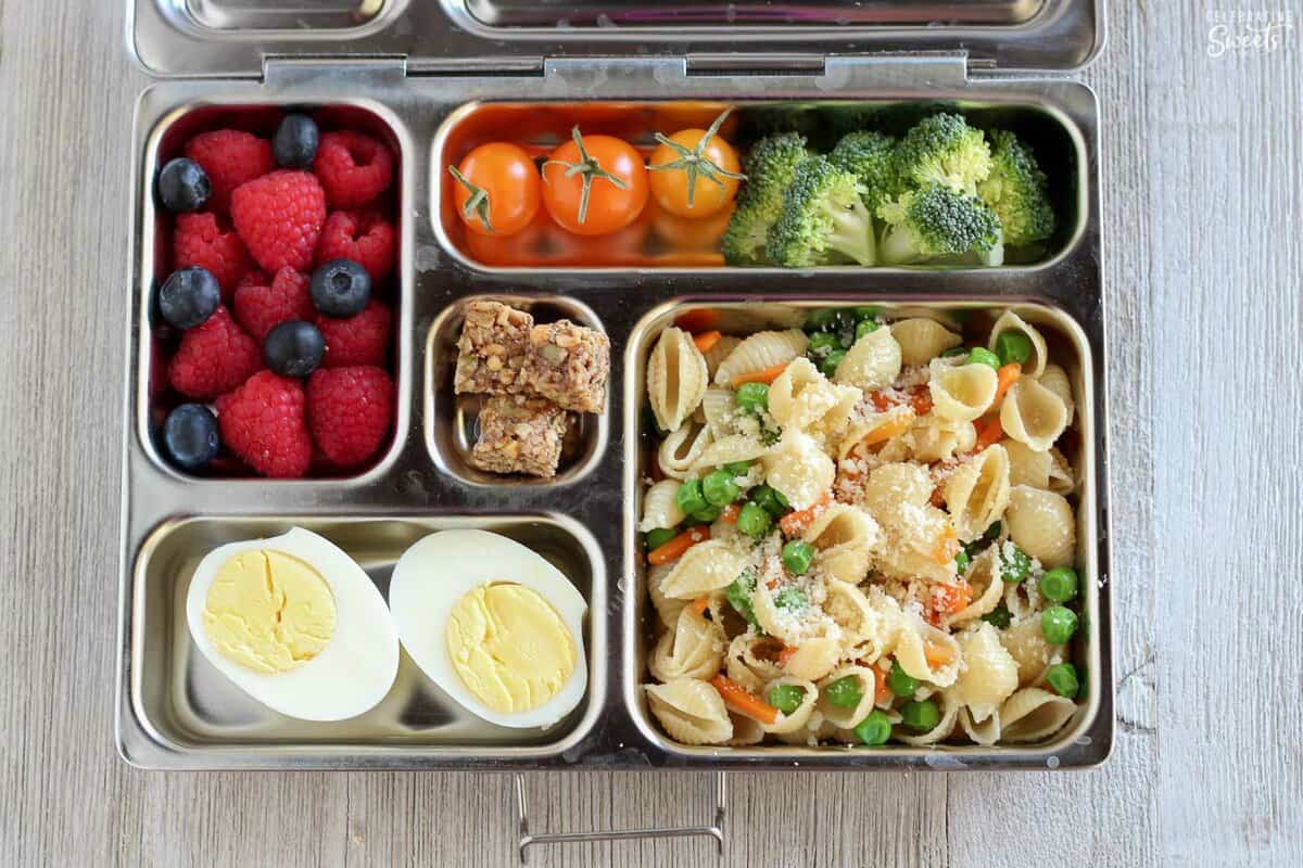Lunchbox filled with pasta salad, hard boiled egg, fruit, and vegetables.