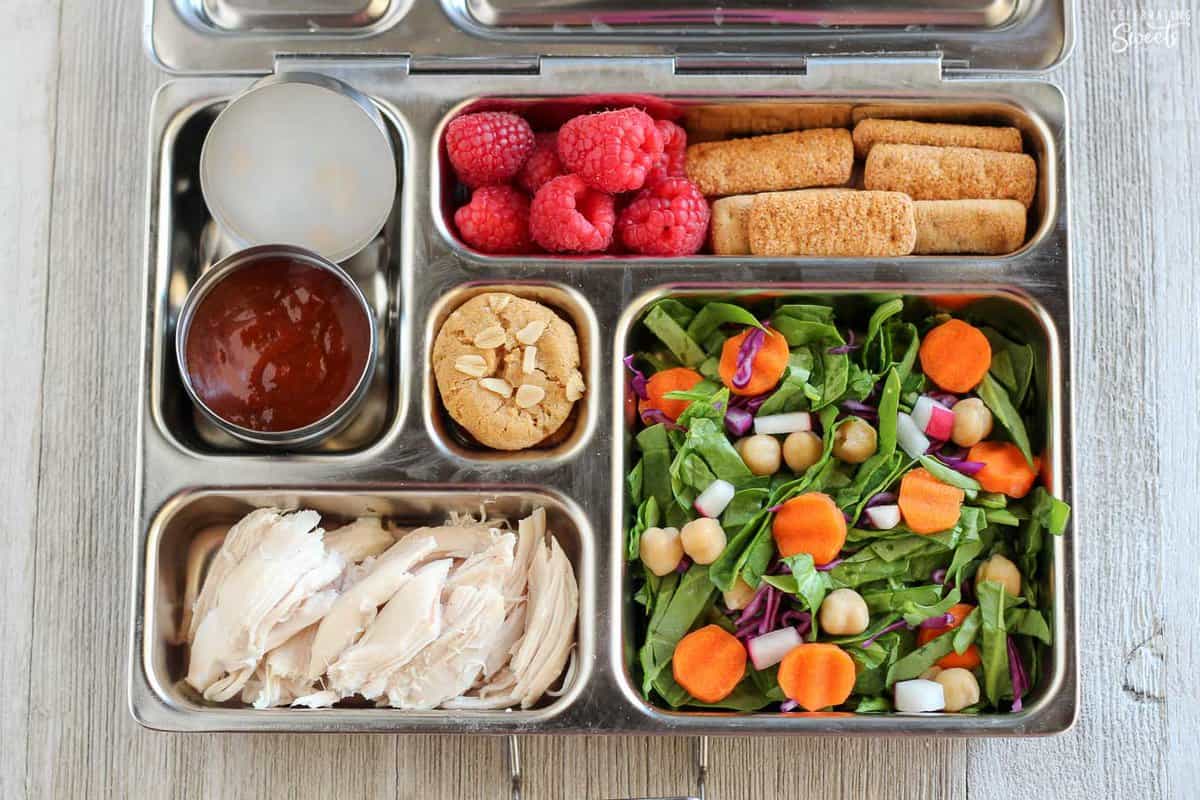 Lunchbox filled with salad, chicken, fruit, crackers.