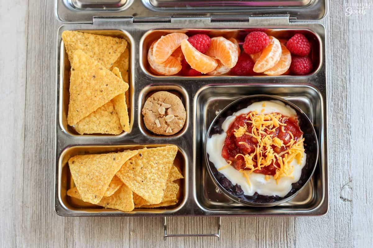 Lunchbox filled with black beans, tortilla chips, and fruit.