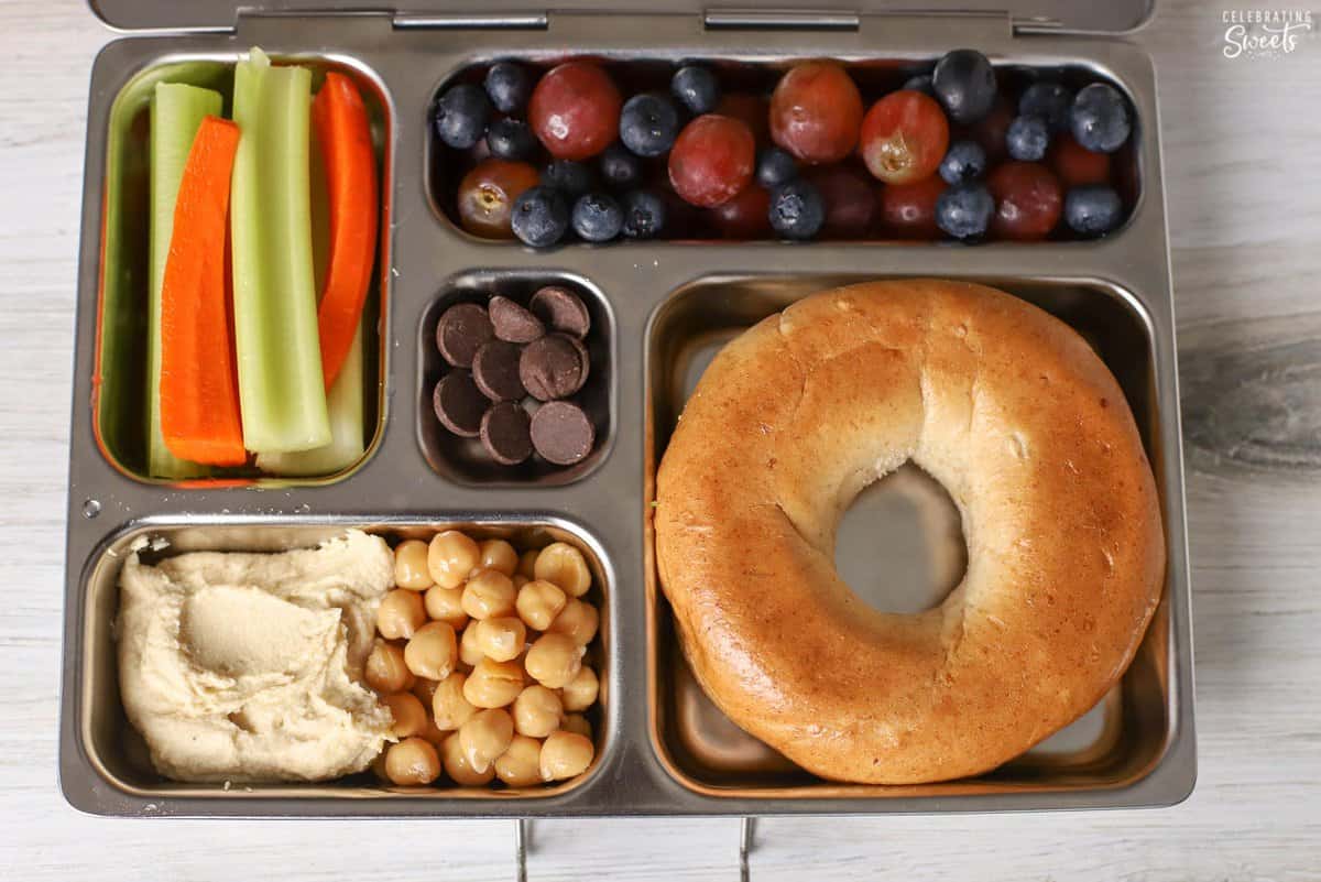 Lunchbox filled with a bagel, chickpeas, hummus, vegetables.
