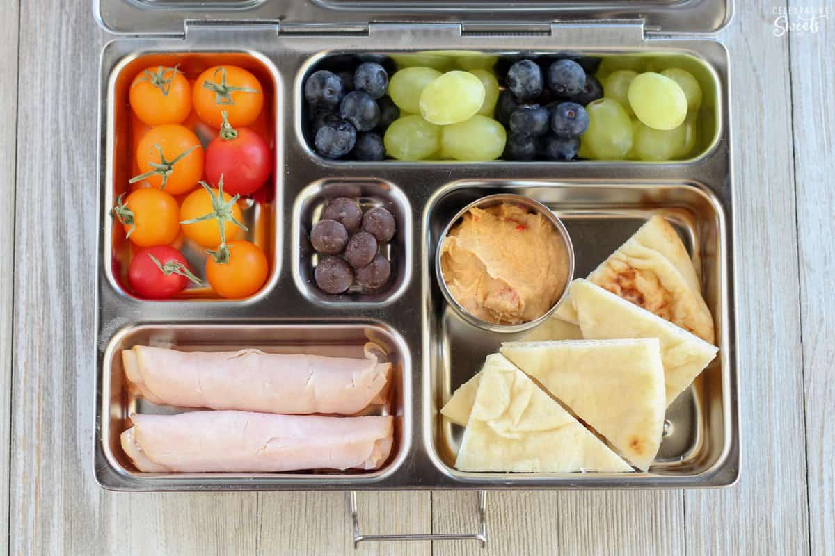 Lunchbox with pita, hummus, turkey, and fruit.