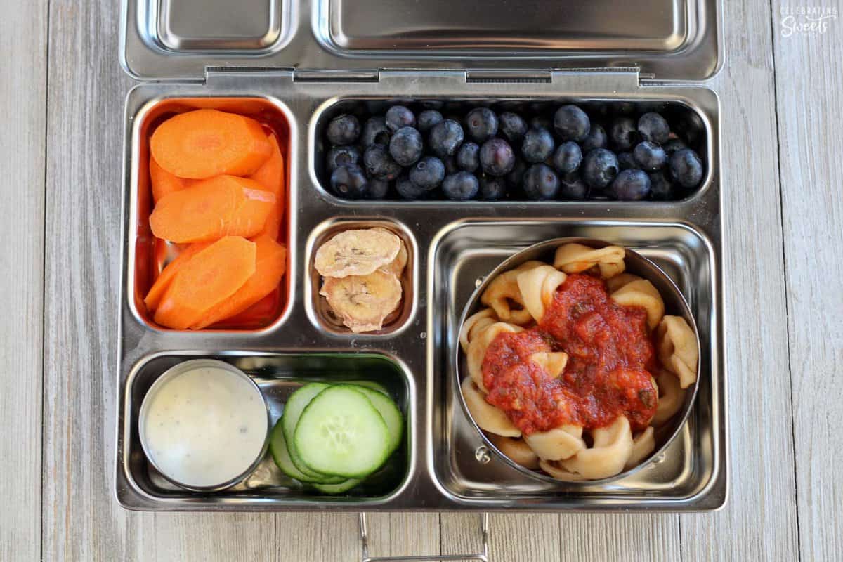 Lunchbox filled with tortellini, vegetables, fruit.