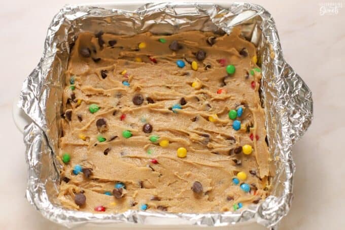 M&M cookie dough in a foil-lined baking dish.