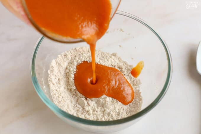 Pumpkin puree being poured into flour in a glass bowl.